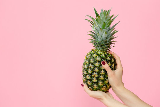 female hands holding pineapple on pink background