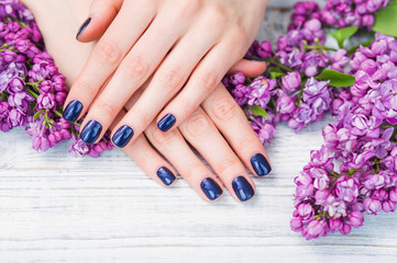 Beauty treatment, woman hands with dark blue manicure and beautiful fresh lilac flowers