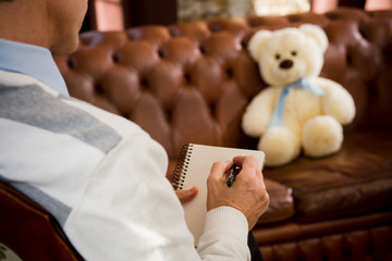 Psychology concept. Psychiatrist man listening to his patient toy bear and writing his...