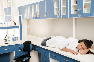 young tired girl scientist sleeping on table in chemical laboratory, chemical lab