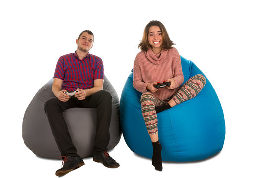 Young man and woman sitting on blue and grey beanbag chairs and playing video games isolated on white background
