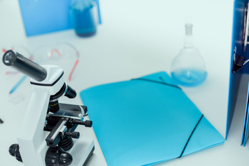 folder, tube with blue reagent and microscope on tabletop in chemical lab