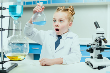 Fototapeta premium schoolgirl in white coat making experiment with reagents in chemical lab, science student concept