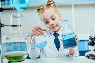 Schoolgirl in white coat making experiment with reagents in science laboratory