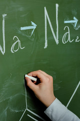 Close-up partial view of schoolchild drawing chemical formula on chalkboard, science school concept