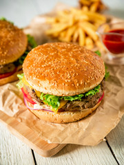 Tasty hamburger with beef, sauce and french fries on wood background. Flat lay. Top view.
