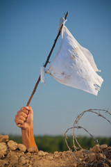 Arm holding stick with a white flag. Soldier in trench with barbed wire surrendering in war battle.