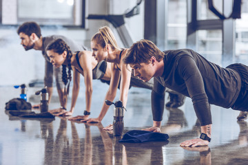 group of athletic young people in sportswear doing push ups or plank at the gym, group fitness concept
