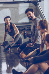 group of athletic young people in sportswear sitting on floor and resting at the gym, group fitness concept