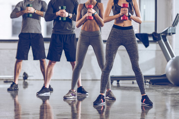 group of athletic young people in sportswear with dumbbells exercising at the gym
