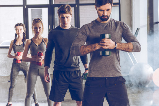 Group of athletic young people in sportswear with dumbbells exercising at the gym