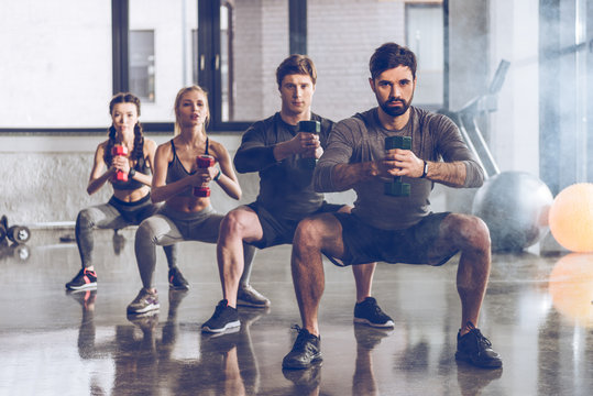 Group Of Athletic Young People In Sportswear With Dumbbells Exercising At The Gym