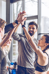 Happy young athletic people in sportswear giving high five in gym