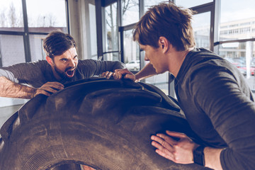 side view of men pulling tire together while exercising at the gym