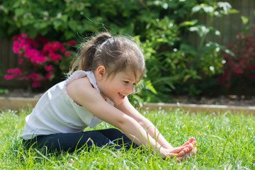 Little girl sitting on the grass in the park doing yoga, reaching her toes, selective focus