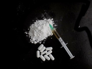 Injection syringe on cocaine drug powder, pills on black background