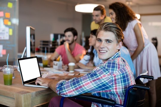 Smiling man using laptop while working with his team in office