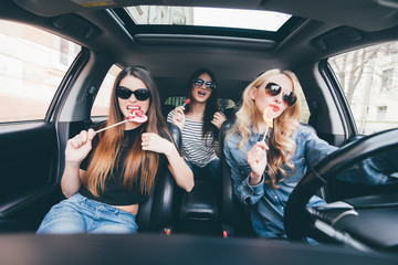 Young women friends with candy have fun when drive new car in road trip