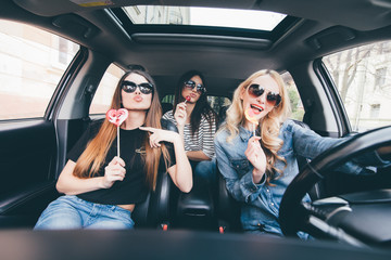 Young women friends with candy have fun when drive new car in road trip