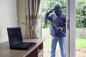 Thief looking through patio doors window at a laptop computer to steal