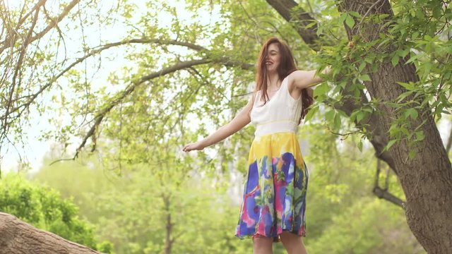 young beautiful girl climbed a tree and walked along a wide branch. Brunette in a bright dress is having fun.