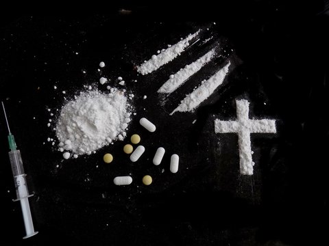 Cocaine drug powder pile, lines and cross, pills and injection syringe on black background