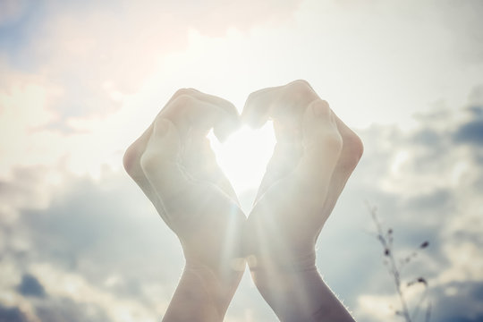Woman making heart shape with hands against clouds