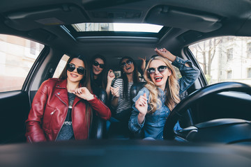 Four beautiful young cheerful women looking at each other with smile while sitting in car