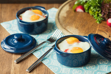 Baked eggs for breakfast in blue ceramic baking molds. Portioned casserole from vegetables and eggs in Italian style. Eggs Kokot