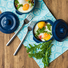 Baked eggs for breakfast in blue ceramic baking molds. Portioned casserole from vegetables and eggs in Italian style. Eggs Kokot. Top view