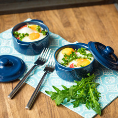 Baked eggs for breakfast in blue ceramic baking molds. Portioned casserole from vegetables and eggs in Italian style. Eggs Kokot