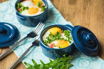 Baked eggs for breakfast in blue ceramic baking molds. Portioned casserole from vegetables and eggs in Italian style. Eggs Kokot