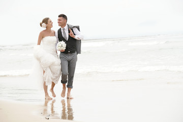 Happy bride and groom walking barefoot on the beach by the sea