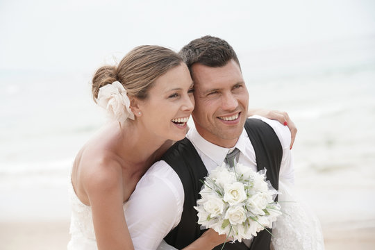 Groom giving piggyback ride to bride on the beach