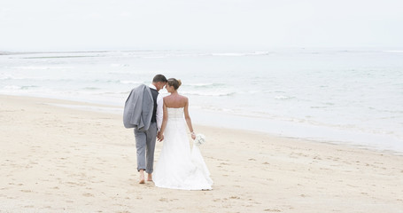Fototapeta na wymiar Back view of bride and groom walking on the beach