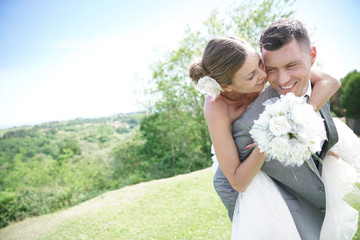 Groom giving piggyback ride to bride in countryside