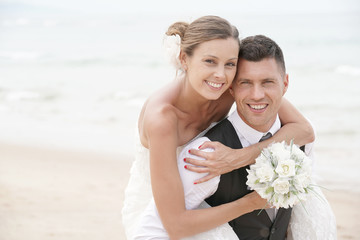 Groom giving piggyback ride to bride on the beach