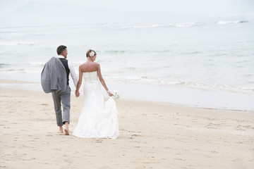 Back view of bride and groom walking on the beach