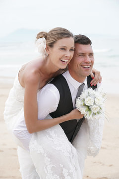 Groom giving piggyback ride to bride on the beach