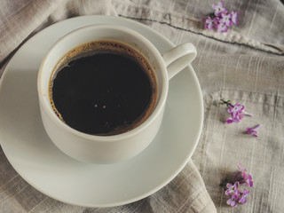 A cup of coffee on the table and lilac flowers