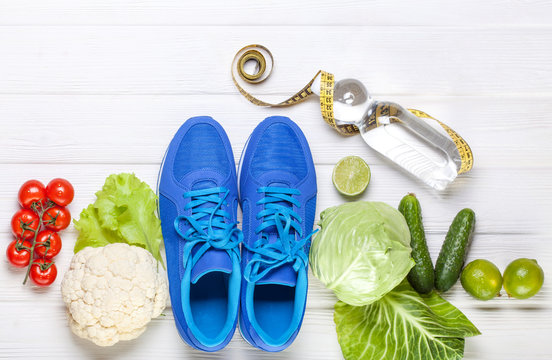 Fresh healthy vegetables, sneakers on white wood background.
