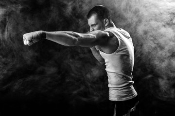 Muscular kickbox or muay thai fighter punching in smoke.