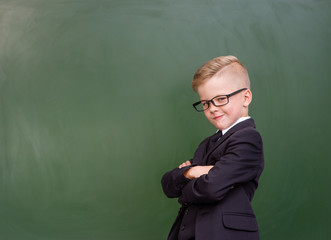 Young boy with crossed arms standing near chalkboard