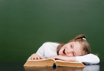 Tired girl lying on the book in classroom