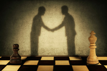 Chess pawn and king standing in front one another with their shadow transform into businessman giving handshake. Business hierarchy levels peace concept.