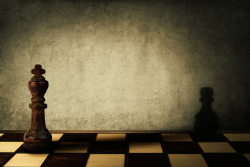 King chess piece casting a shadow of a pawn on a concrete wall. Complex and mismanagement concept....
