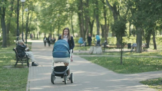 Young mother with pram walks in the green park