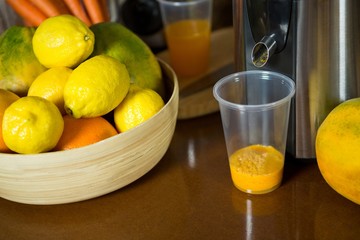 Lemons on wooden bowl with glass of juice at counter