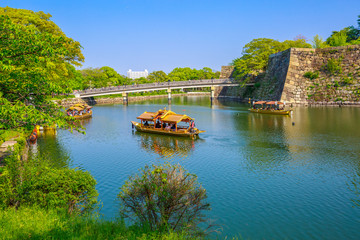 Tourist boats along the moat and the wall of Osaka Castle while crossing the popular Gokurakubashi Bridge or Gokuraku Bridge leading to Osaka Castle Park. Osaka city, Japan.