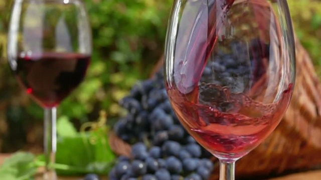 Red wine is poured into a glass on a background full glass and of a basket of ripe grapes